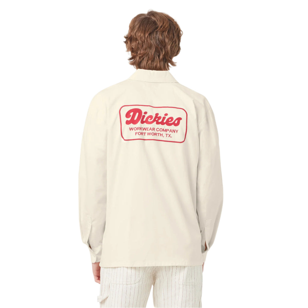 Person wearing a cream-colored shirt with a red logo on the back, standing against a white background